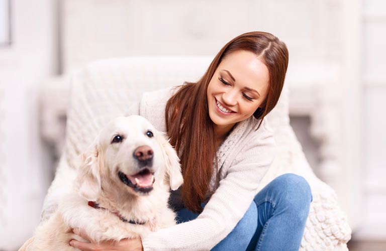 A smiling woman with brown hair sitting with and holding her happy big white dog